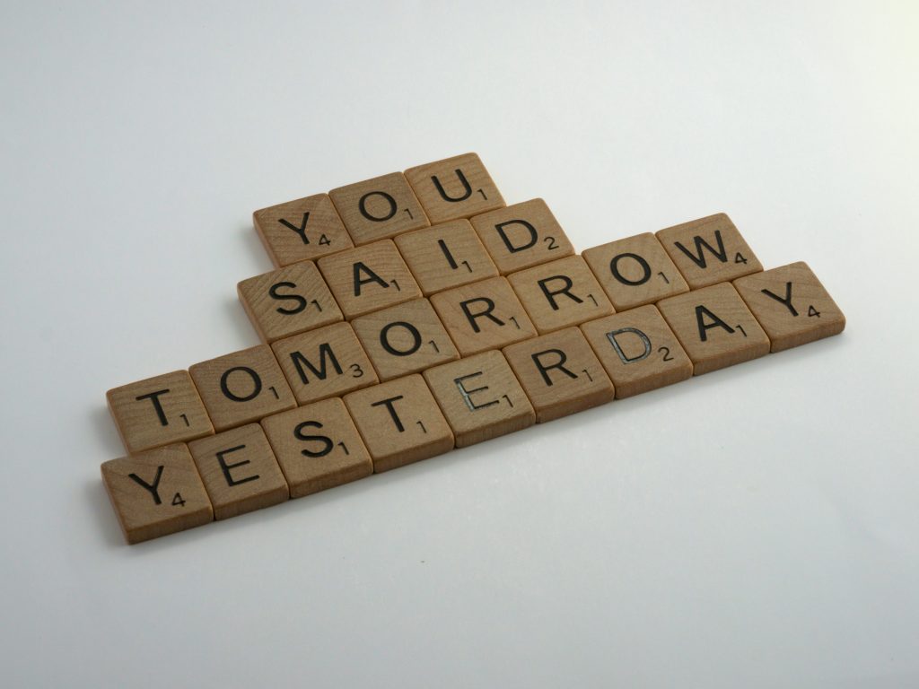 Scrabble tiles arranged on a white surface spell out “You said tomorrow yesterday” in a staggered layout.